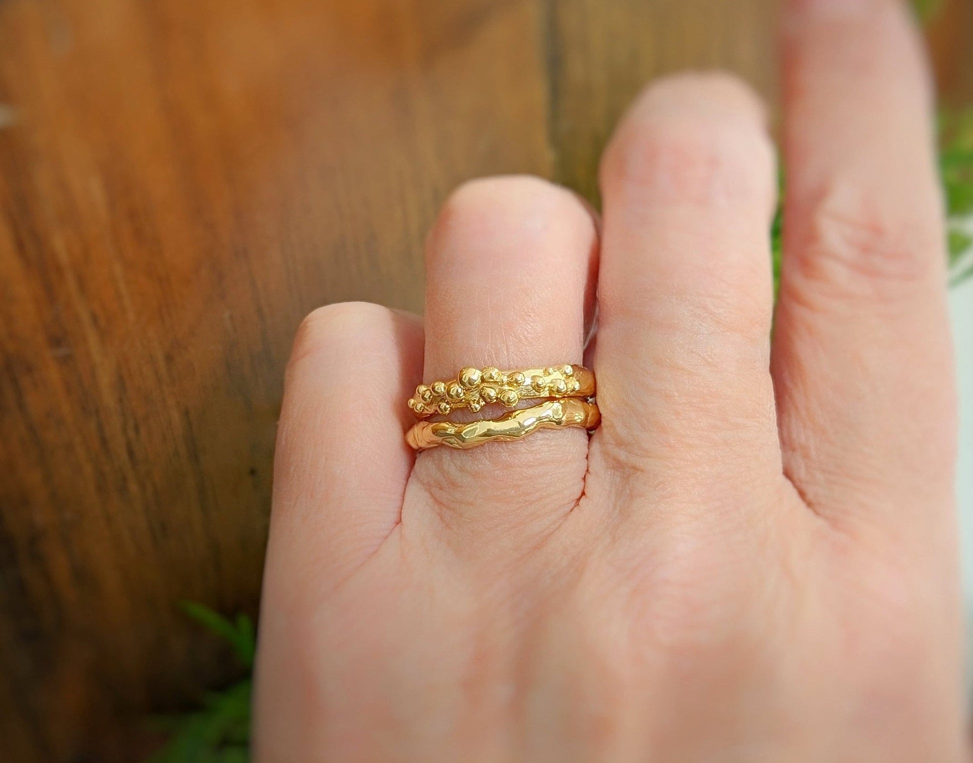 Hand wearing 2 Molten Gold wedding bands, showcasing their unique organic textures and golden shine.