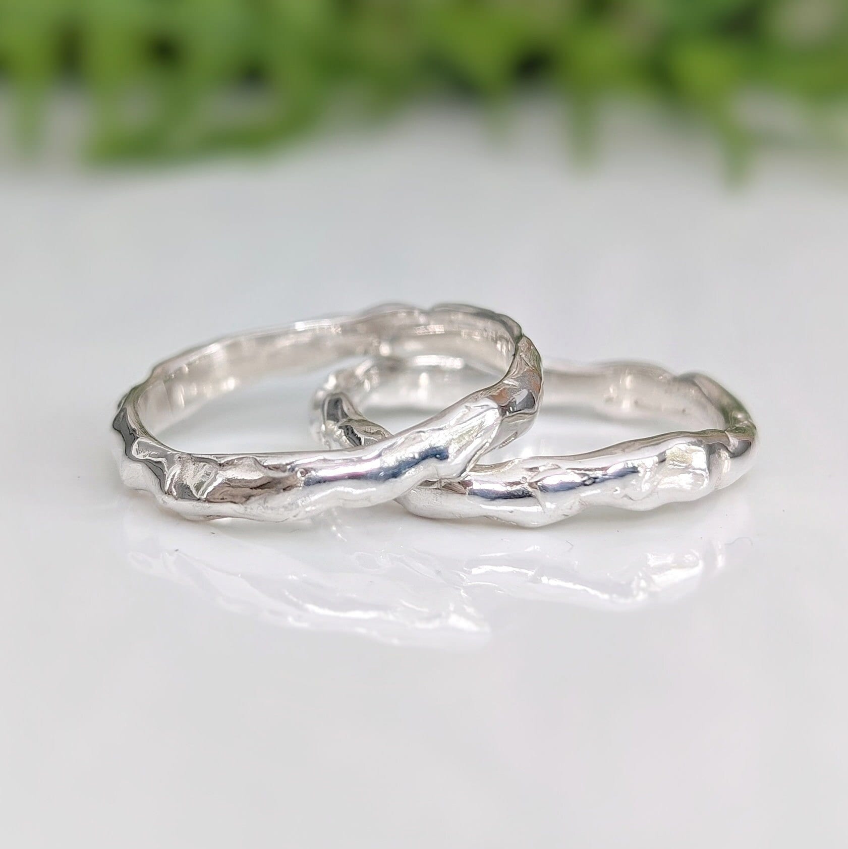 Two handcrafted Molten Silver wedding bands showcasing unique organic texture and elegance on a reflective surface.