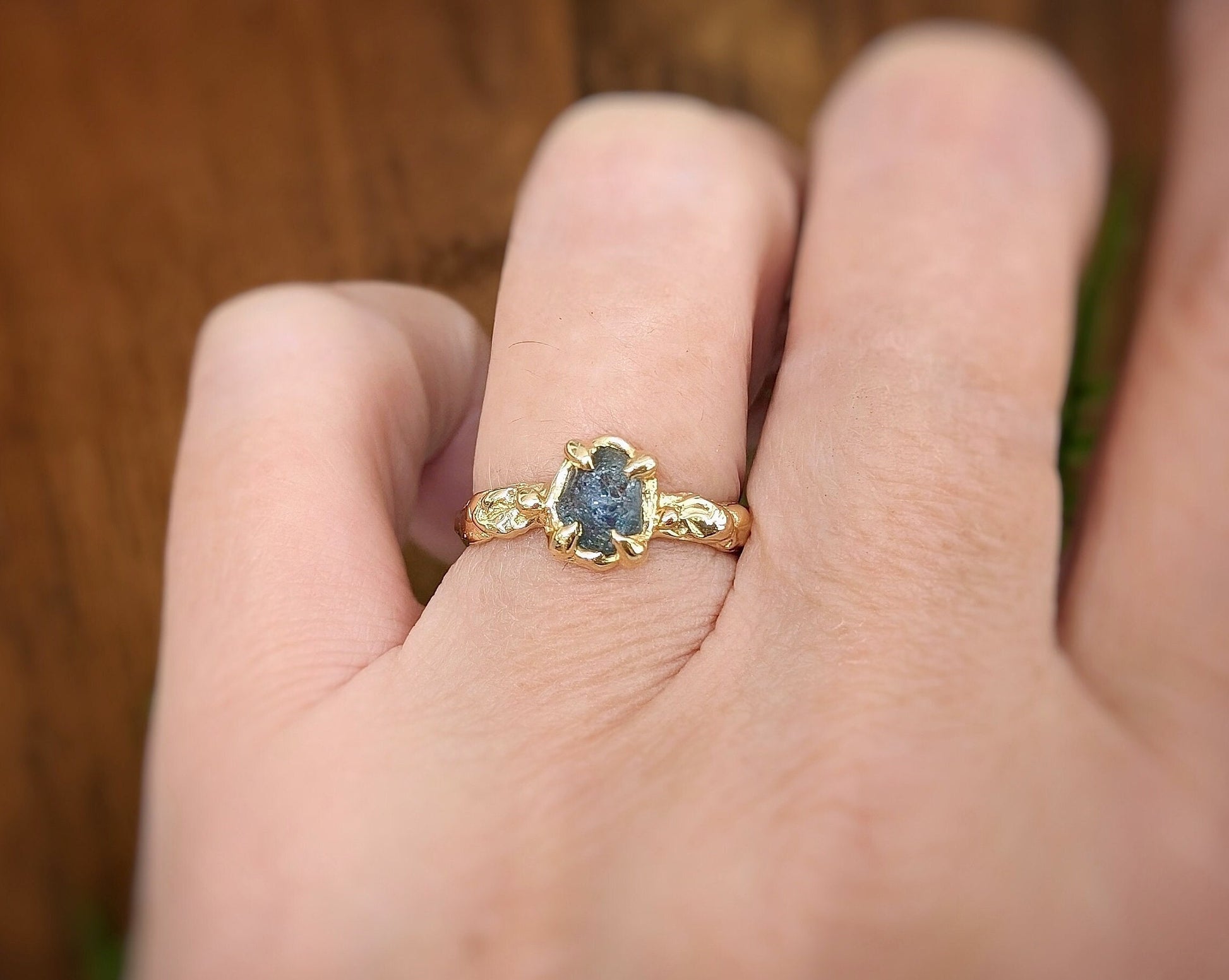 Hand wearing a Raw Montana Sapphire set by prongs on a textured Solid 14k Gold band