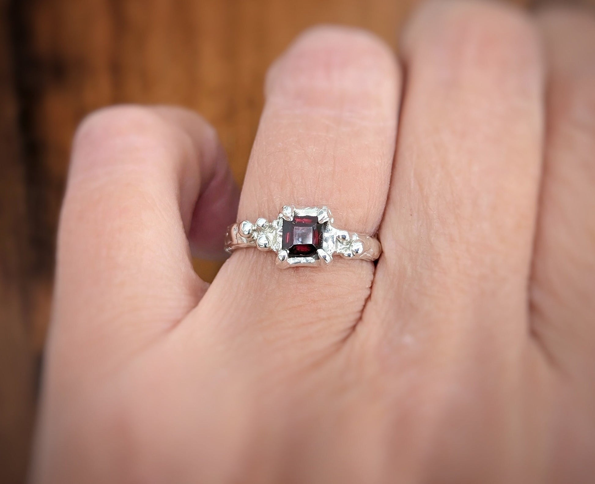 Woman's hand wearing a Square Red Garnet set on a Molten Silver textured band