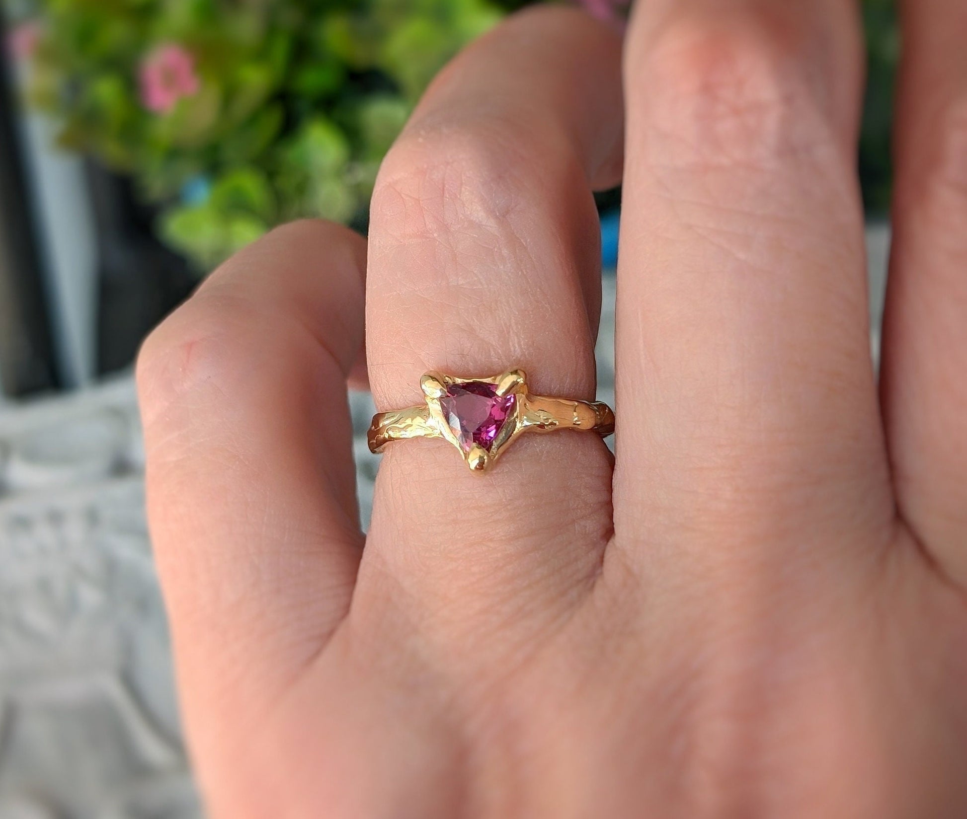 Hand with a Trilliant shape Rubellite Tourmaline set by prongs on a textured Solid 14k Gold band