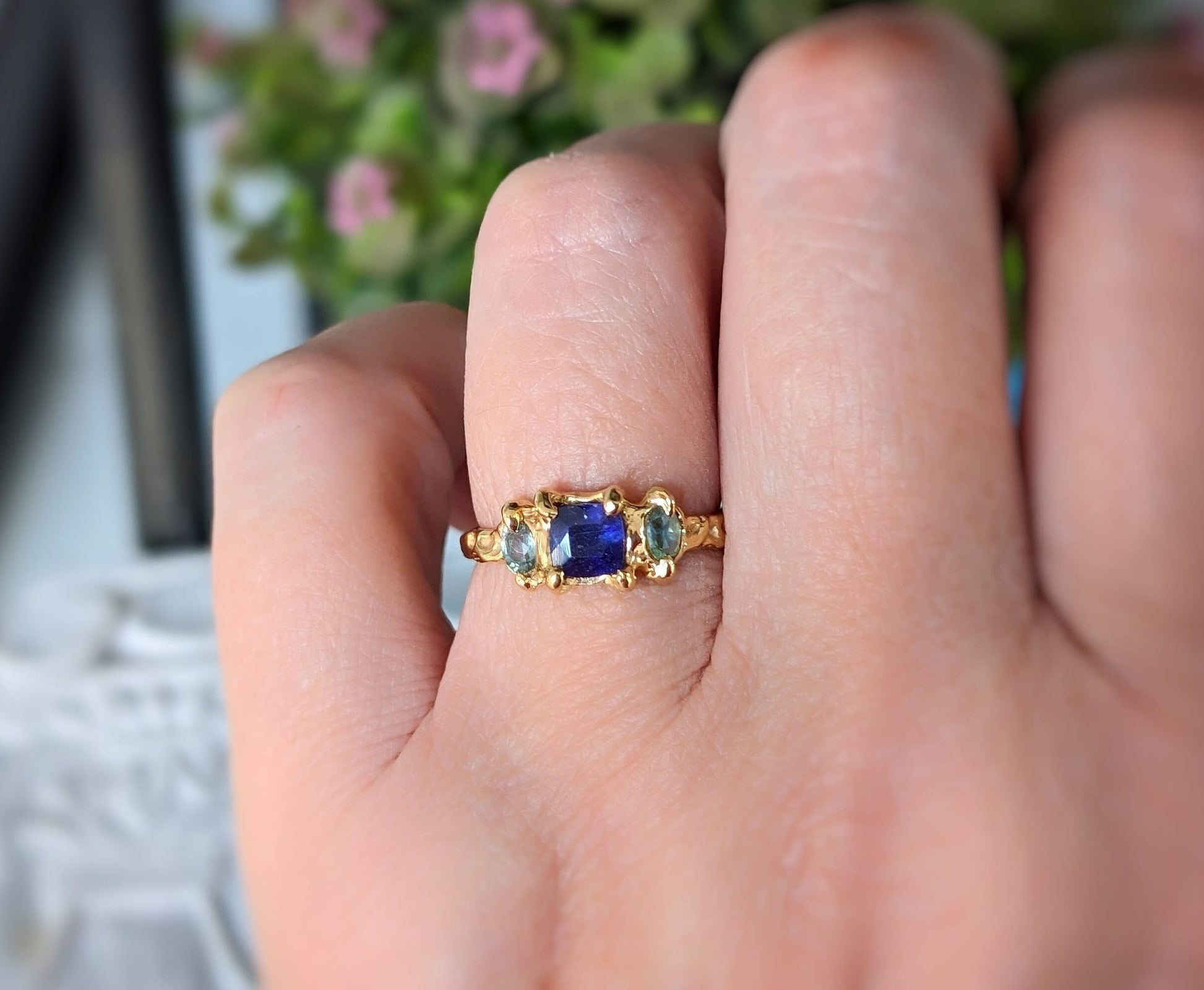 Woman's hand wearing a Blue Sapphire and Tourmaline ring in textured molten Gold setting