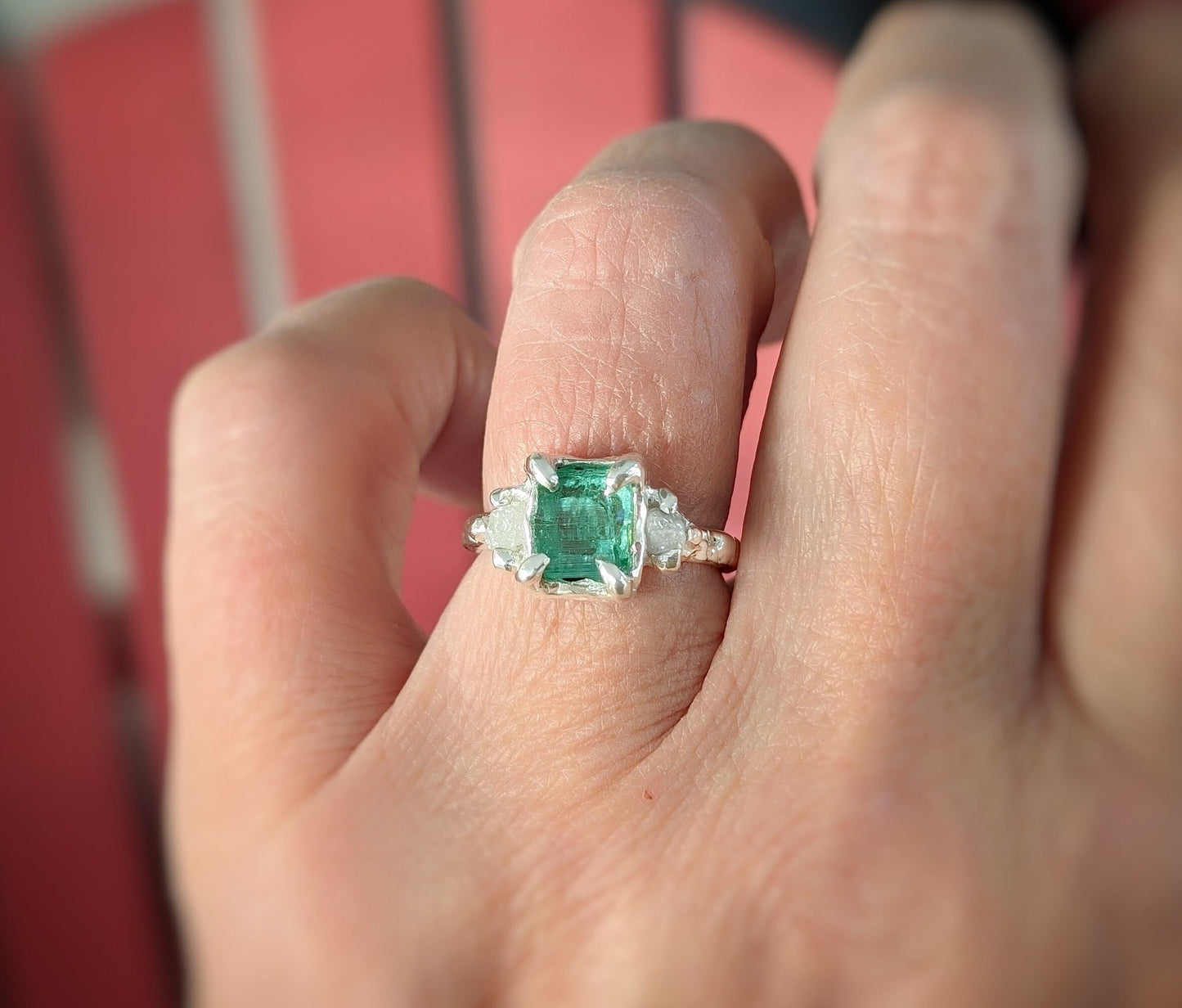 Woman's hand wearing  a Raw mint green Emerald and diamonds set on Molten Silver prong setting